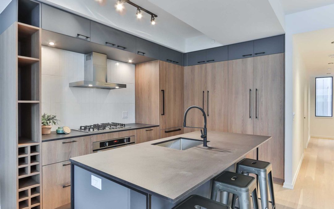 Modern kitchen with wood cabinets, island sink, black stools, and built-in stove under a sleek range hood.