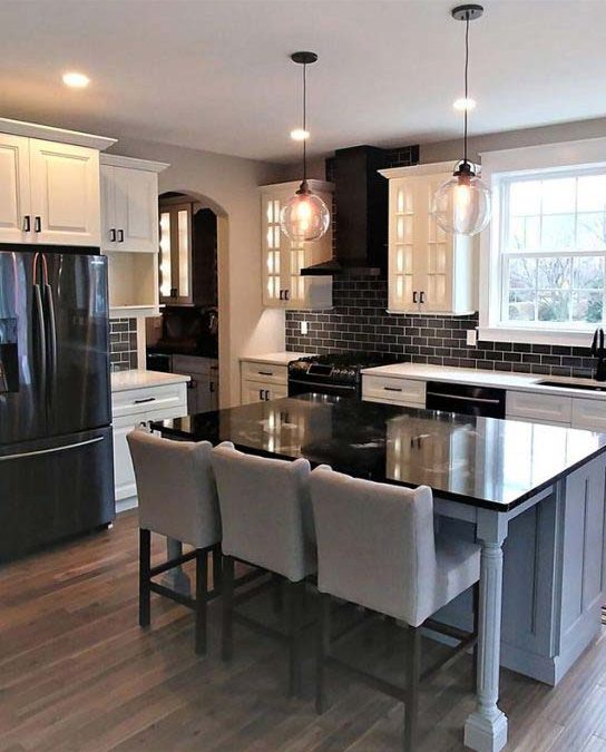 Modern kitchen with black granite island, pendant lights, white cabinets, black appliances, and cushioned chairs.
