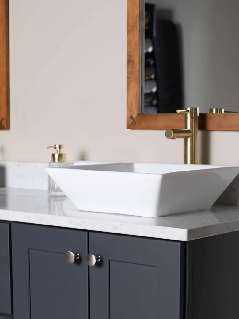 Modern bathroom vanity with a white square vessel sink, gold faucet, and dark cabinetry.