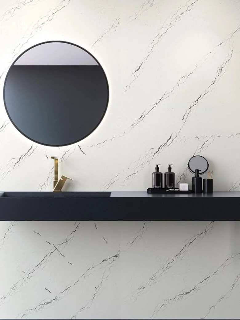Modern bathroom with a round mirror, black sink counter, and marble-patterned wall with toiletries on the counter.