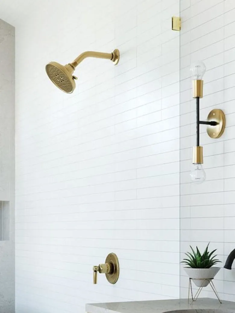 Modern bathroom with white subway tile, brass shower fixtures, a wall sconce, and a small potted plant on the counter.