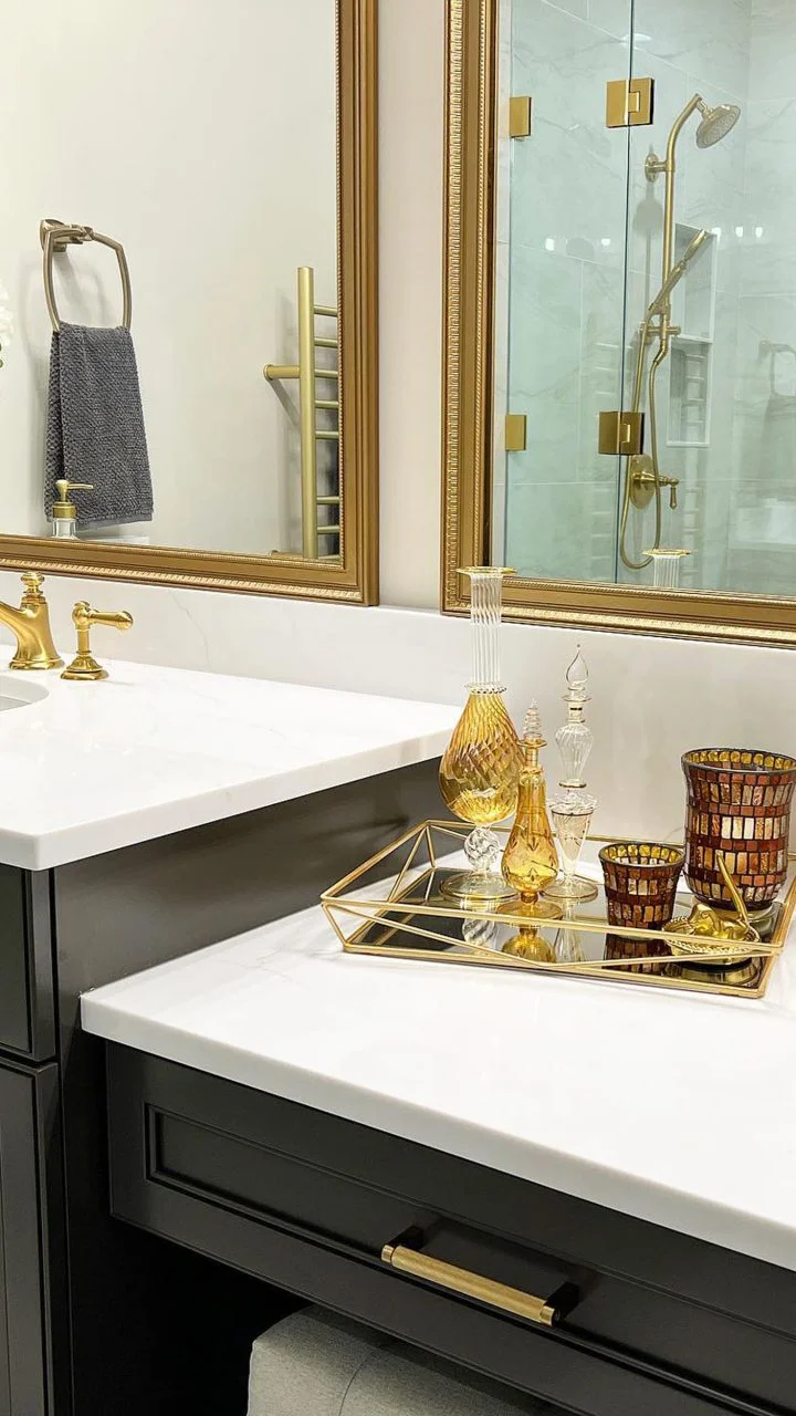 Elegant bathroom counter with gold decor, glass bottles, and gold accents near a modern shower and mirror.