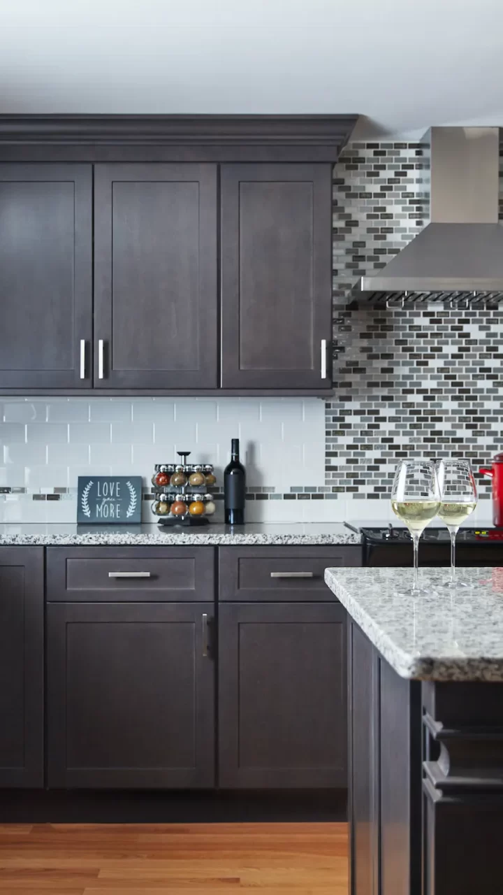 Modern kitchen with dark cabinets, mosaic tile backsplash, and two glasses of white wine on the counter.