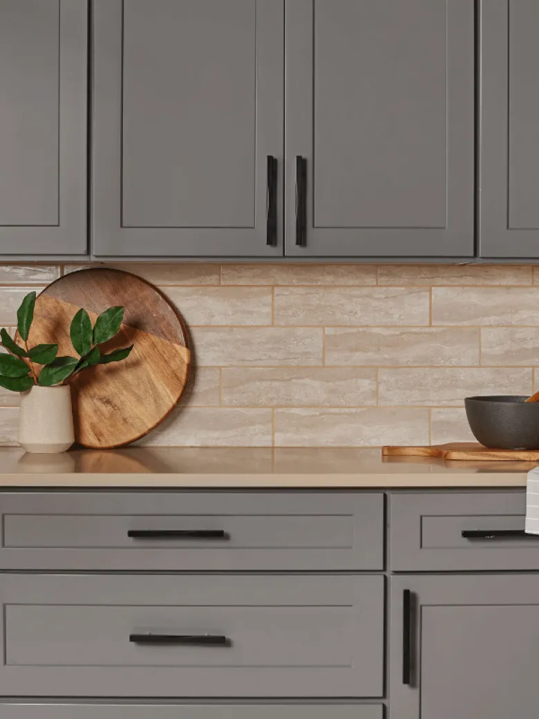Modern kitchen with gray cabinets, beige subway tile backsplash, and wood accessories on the countertop.