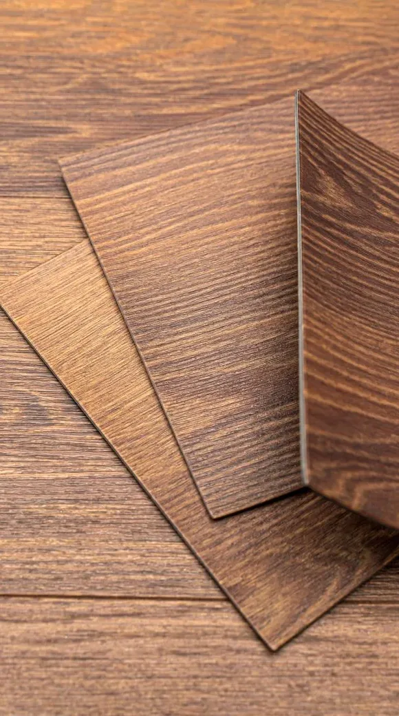 Three sheets of brown wood-patterned laminate flooring overlapping on a matching wood surface.